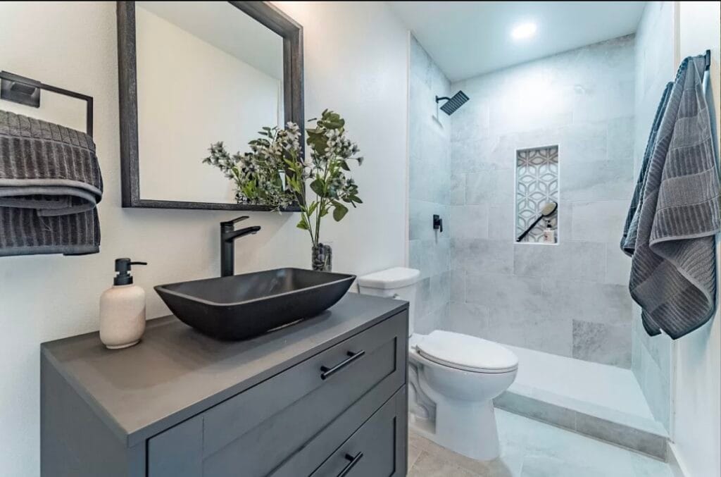 Baño renovado por BMI Design & Decor con lavabo, espejo de madera y ducha de azulejos en Texas.